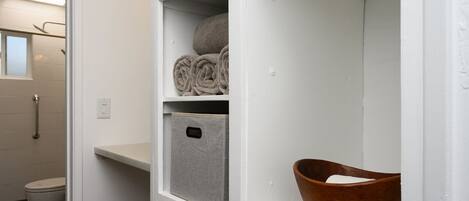 A bathroom with a toilet, a shower, and a shelf with towels and a storage box.