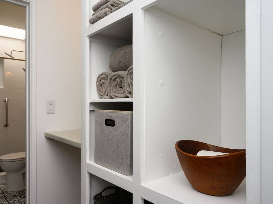 A bathroom with a toilet, a shower, and a shelf with towels and a storage box.