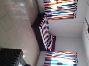 Una habitación con piso de baldosas, una cama con ropa de cama a rayas y una mesita.