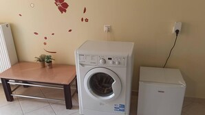 Una habitación compacta con lavadora, un refrigerador pequeño y una mesa de madera.