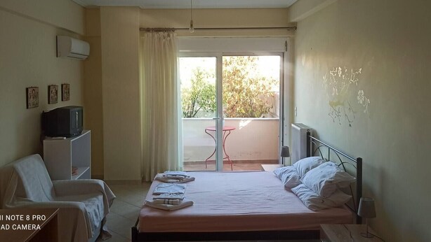 Habitación de hotel con cama, una silla, una mesita, televisor y balcón con mesa y sillas.