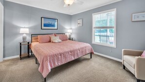 A bedroom with a bed, two bedside tables, a ceiling fan, a window with blinds, and a chair.