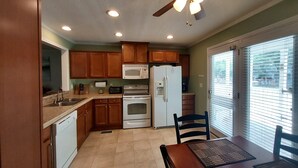 A kitchen with wooden cabinets, a microwave, an oven, a refrigerator, and a dining area with a table and chairs.