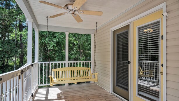 A covered porch with a wooden bench, a ceiling fan, and a sliding glass door with blinds.