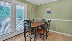 A dining room with a wooden table and chairs, a ceiling fan, a clock, and a framed picture on the wall.