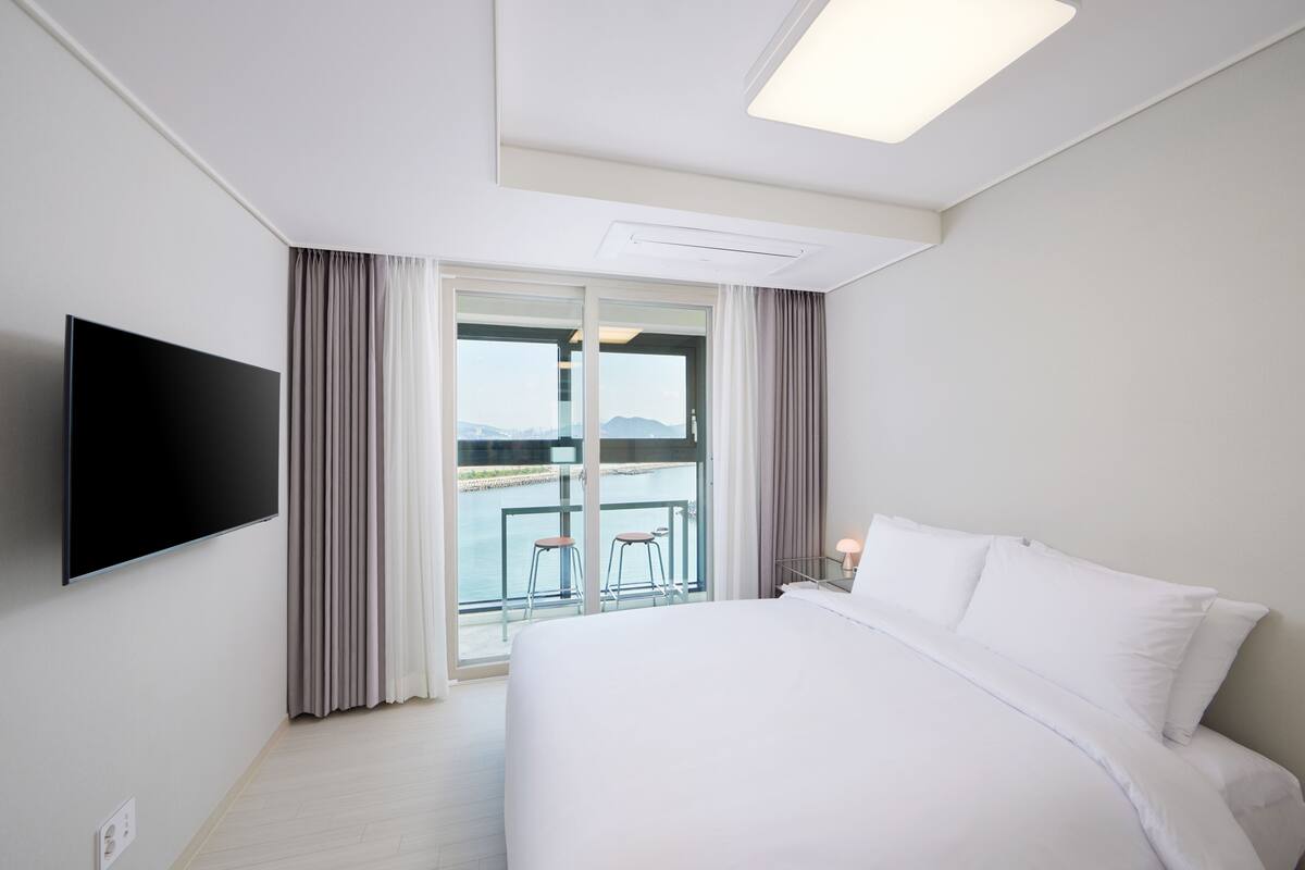A hotel room with a bed, a TV, a balcony with a view, and a window with curtains.