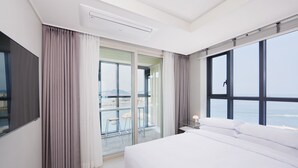 A modern hotel room with a large bed, a balcony with a view of the sea, and a sliding glass door. - Shift Door Residence Hari (Busan)