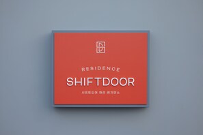 A red sign with the words "RESIDENCE SHIFT DOOR" and a small icon above it. - Shift Door Residence Hari (Busan)
