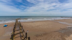 A beach with a wooden walkway leading to the water, a blue tent, and people on the sand. - Birch Cottage, Northrepps, Norfolk (Northrepps)