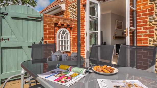 An outdoor seating area with a glass table, a newspaper, and a plate of cookies. - Birch Cottage, Northrepps, Norfolk (Northrepps)