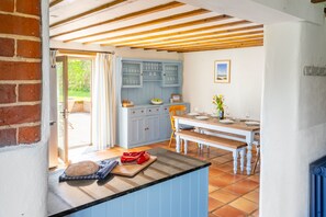 Uma cozinha com um banco de madeira, um armário azul e uma mesa de jantar posta para quatro pessoas.