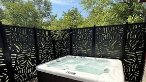 Un jacuzzi rodeado por una valla negra con diseños de hojas, ubicado en un jardín con árboles al fondo.