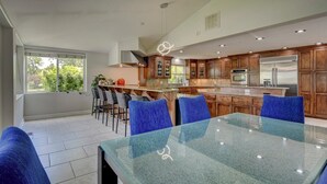 Una cocina moderna con una isla central, taburetes de bar y una mesa de comedor con sillas azules.