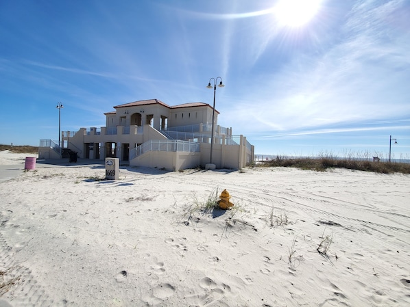 Un bâtiment situé en bord de mer, avec un escalier menant à l’entrée, une borne d’incendie jaune et un ciel dégagé.