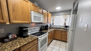 A kitchen with wooden cabinets, a white microwave, a stove, and a refrigerator. - Beach Life Condo 135. Pools! Beach! Casinos! FUN! (Biloxi)