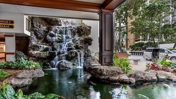 Une cascade ornementale avec un bassin à carpes koï, entourée d’une végétation luxuriante et offrant une vue sur le paysage urbain.