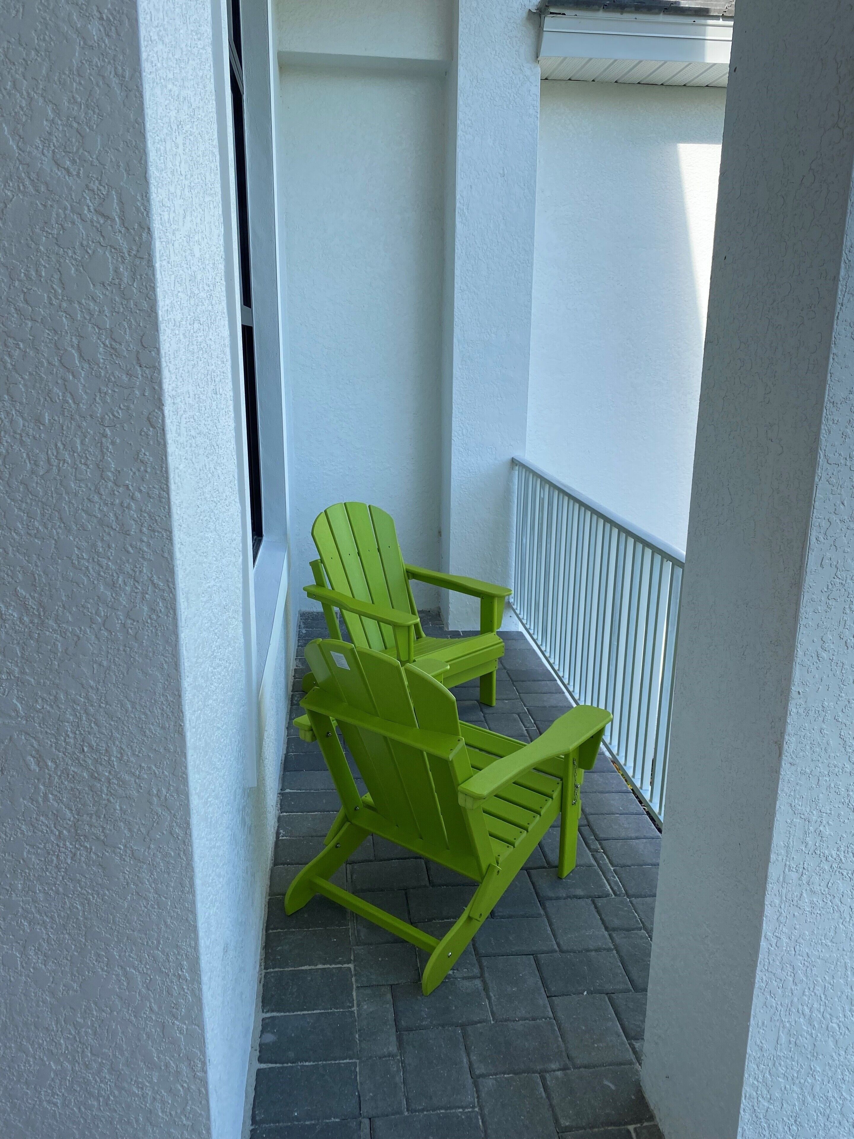 Un balcon avec deux fauteuils Adirondack verts et une balustrade blanche.