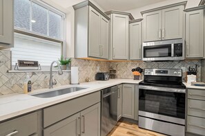 A modern kitchen with grey cabinets, a stainless steel dishwasher, a microwave, and an oven.