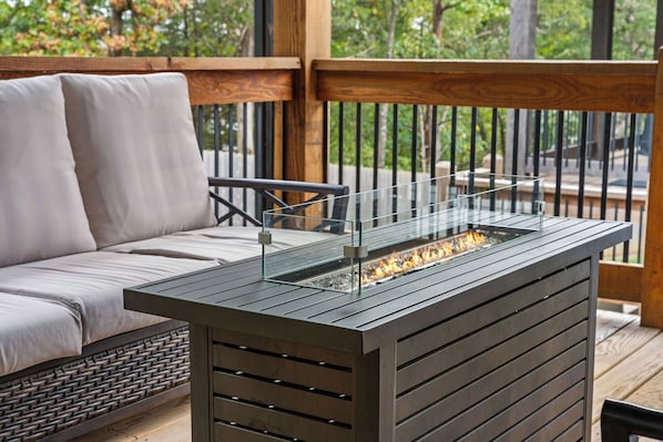 A modern outdoor seating area with a glass-top fire feature, wooden deck, and wicker furniture.