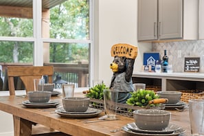Una mesa de comedor dispuesta con platos, tazones y un vaso, con una figurita de oso que lleva un letrero que dice 'WELCOME'.
