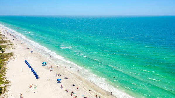 A beach with clear turquoise waters, a sandy shore, and several umbrellas and beach chairs.