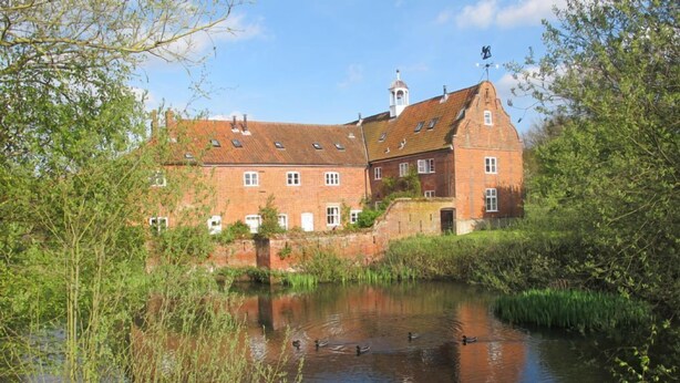 A historic brick building with a river in front, surrounded by greenery. - Waterside Cottage - sleeps 8 guests  in 3 bedrooms (Norwich)
