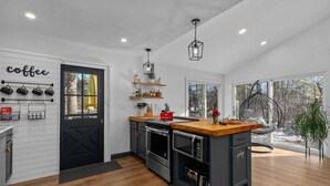 A modern kitchen with a black door, wooden cabinets, and a central island. - Lakefront: Hot Tub, Sauna, Firepit & Pontoon Fun (Wautoma)