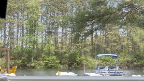 A room with a large window overlooking a lake, a chair, a table, and a television. - Lakefront: Hot Tub, Sauna, Firepit & Pontoon Fun (Wautoma)