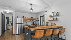 A modern kitchen with a central island, bar stools, wooden shelves, and a refrigerator. - Lakefront: Hot Tub, Sauna, Firepit & Pontoon Fun (Wautoma)