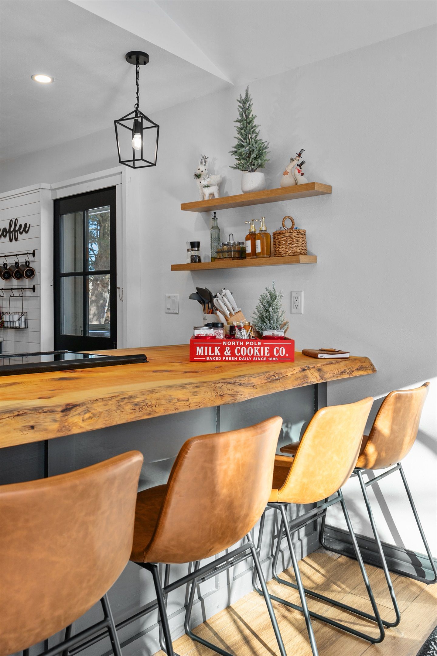 Una cocina con una barra de madera, sillas de cuero marrón y estantes con utensilios de cocina.