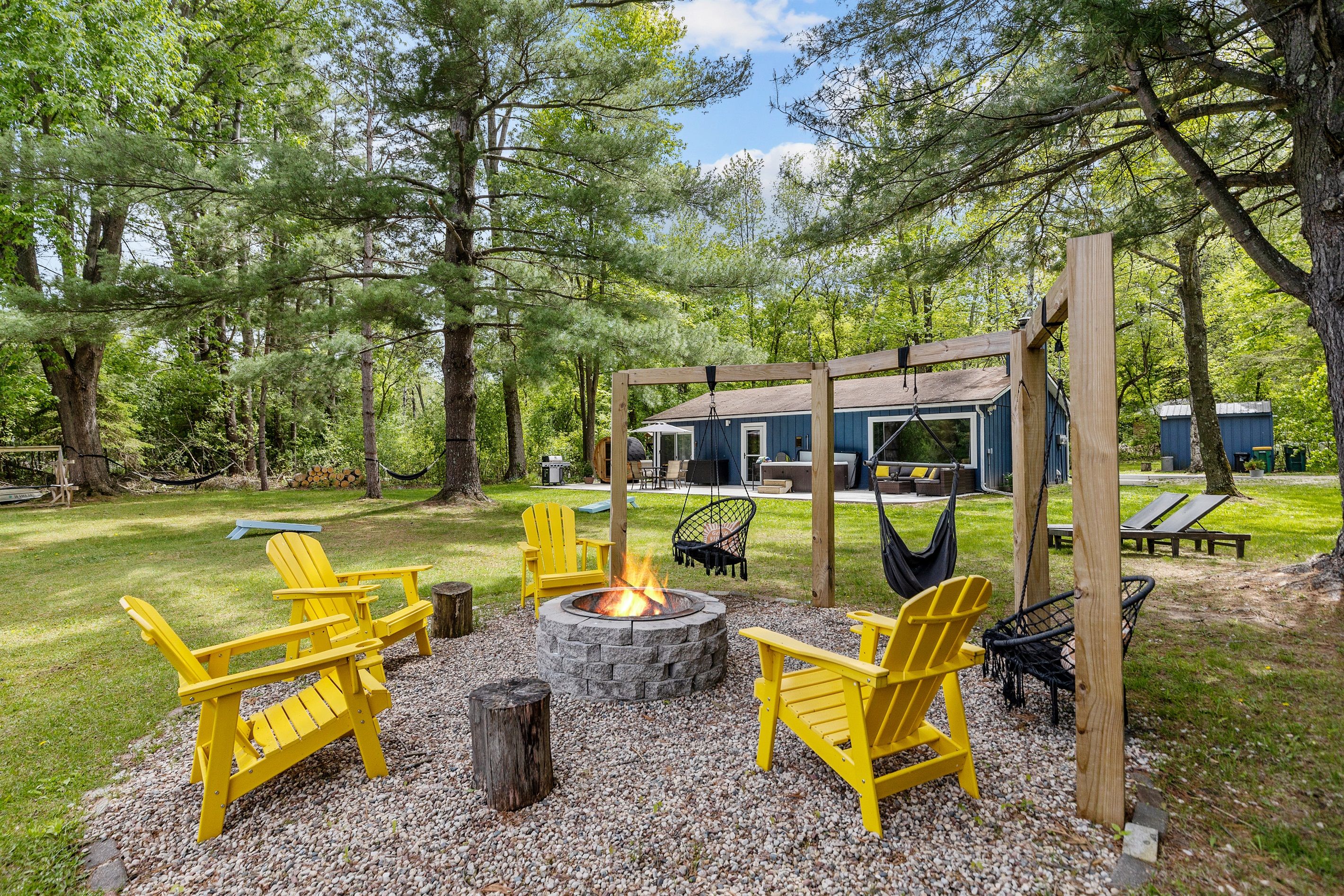 A backyard with a fire pit, Adirondack chairs, a hammock, and a wooden pergola.