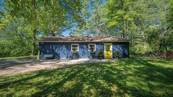 A single-story house with a dark blue exterior, a yellow door, and a small front porch with a bench.