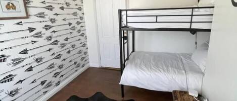 Una habitación con literas, un papel tapiz estampado, un tapete de cuero de vaca y una lámpara colgante.