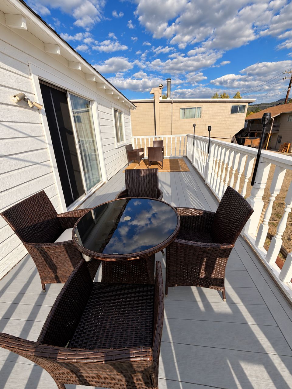 A covered patio with wicker furniture and a glass table, white railings, and a clear sky.