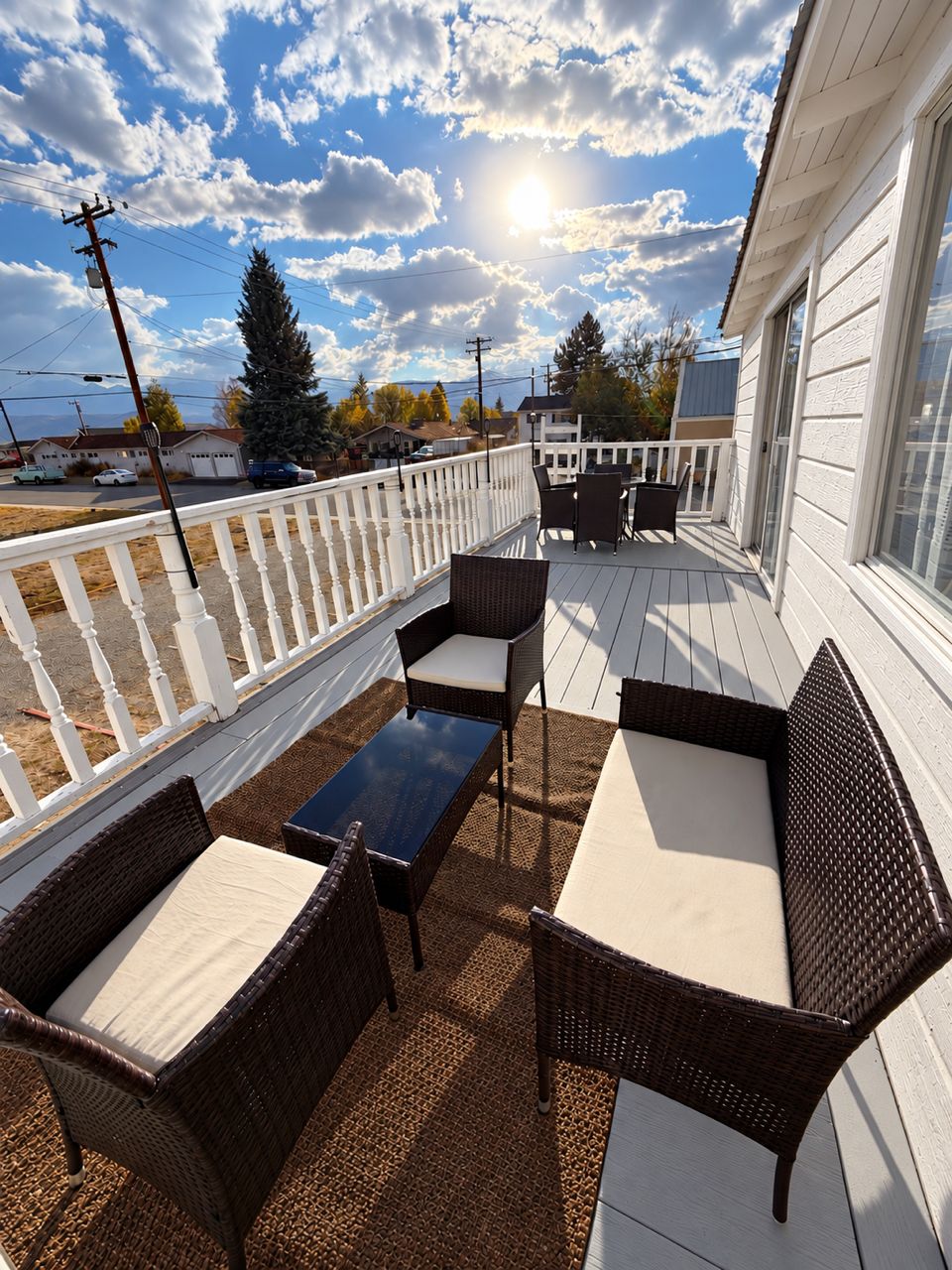 Terraza exterior techada con muebles de mimbre y una mesa, con vista a una calle.