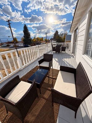 A covered outdoor deck with wicker furniture and a table, overlooking a street. - The Bodie Hotel (Bridgeport)