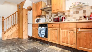 A kitchen with wooden cabinets, a microwave, a toaster, and a dishwasher. - Keepers Cottage (Liskeard)