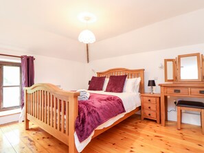 A bedroom with a wooden bed, a nightstand, a desk, and a mirror. - Keepers Cottage (Liskeard)