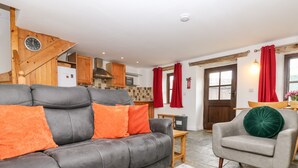 A living room with a grey sofa, orange cushions, a grey armchair, and a wooden coffee table. - Keepers Cottage (Liskeard)