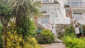 A residential building with a stone facade, multiple balconies, and a garden area with various plants and a bench. - Flat 6 (Falmouth)