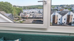 A view from a window overlooking a marina with boats, a small building, and residential buildings in the distance. - Flat 6 (Falmouth)