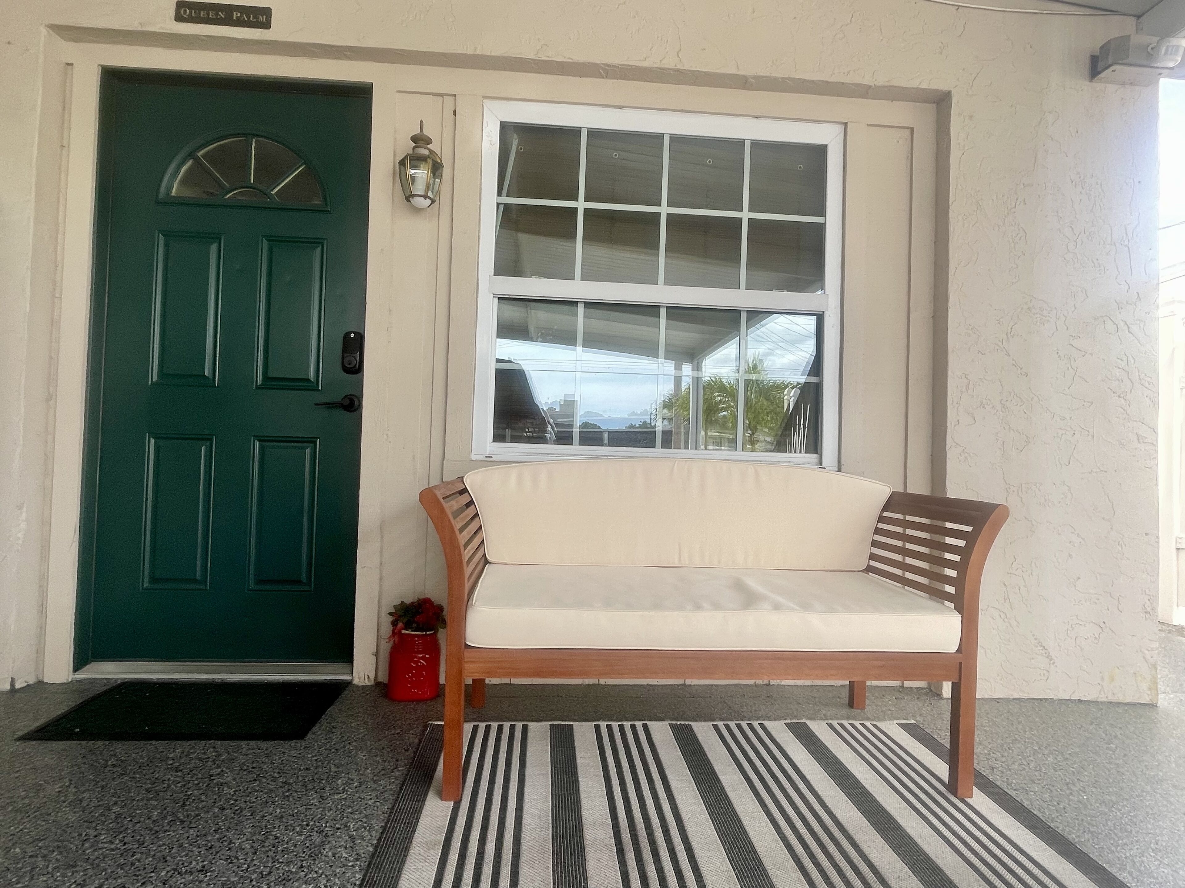 A green door with a nameplate, a white window, and a wooden bench with a cushion.