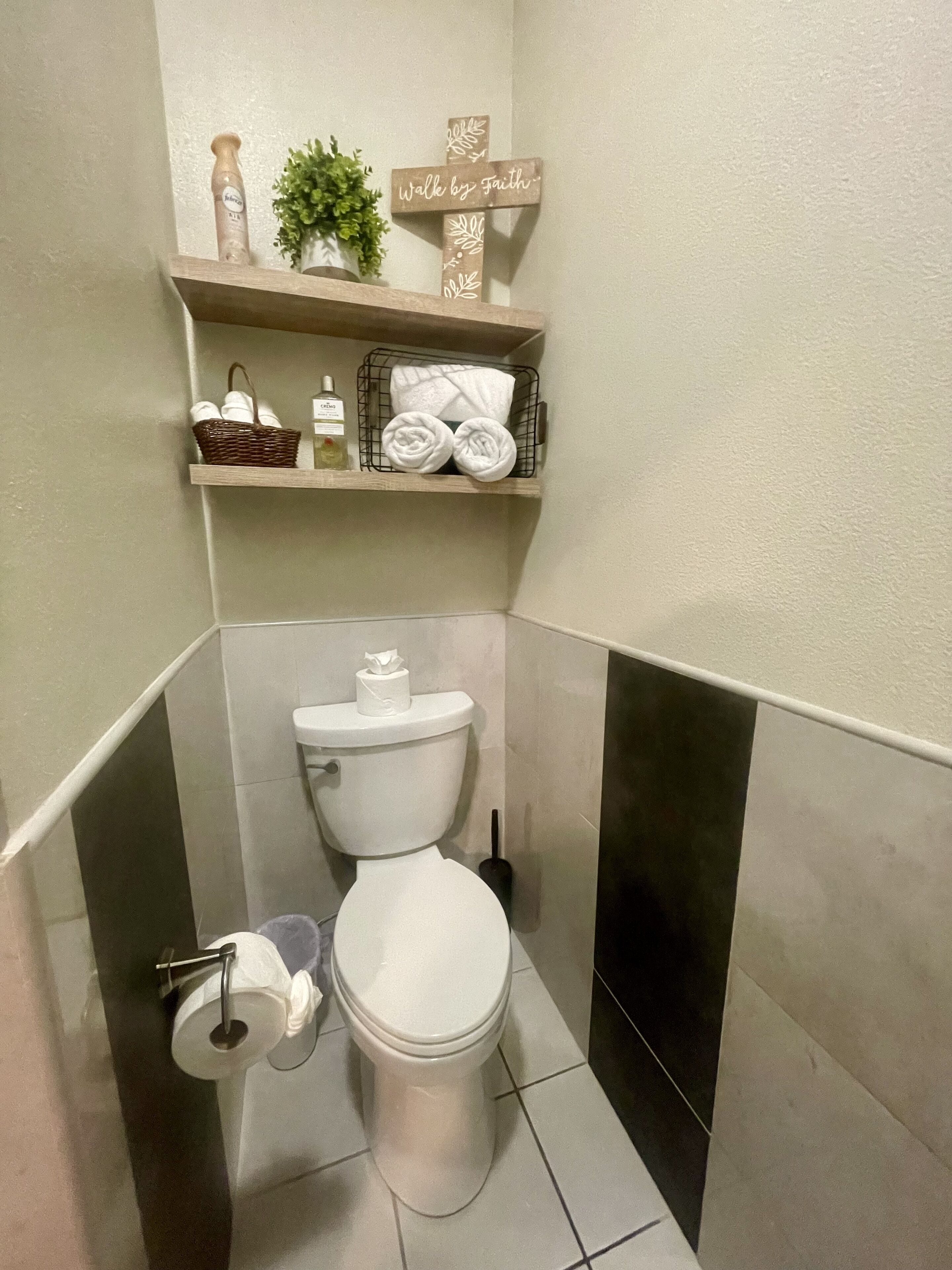 A bathroom with a toilet, a shelf with towels and toiletries, and a decorative sign.