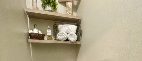 A bathroom with a toilet, a shelf with towels and toiletries, and a decorative sign.