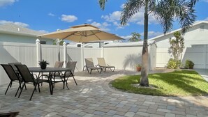 Une terrasse extérieure avec une table et des chaises, un grand parasol et une petite pelouse.