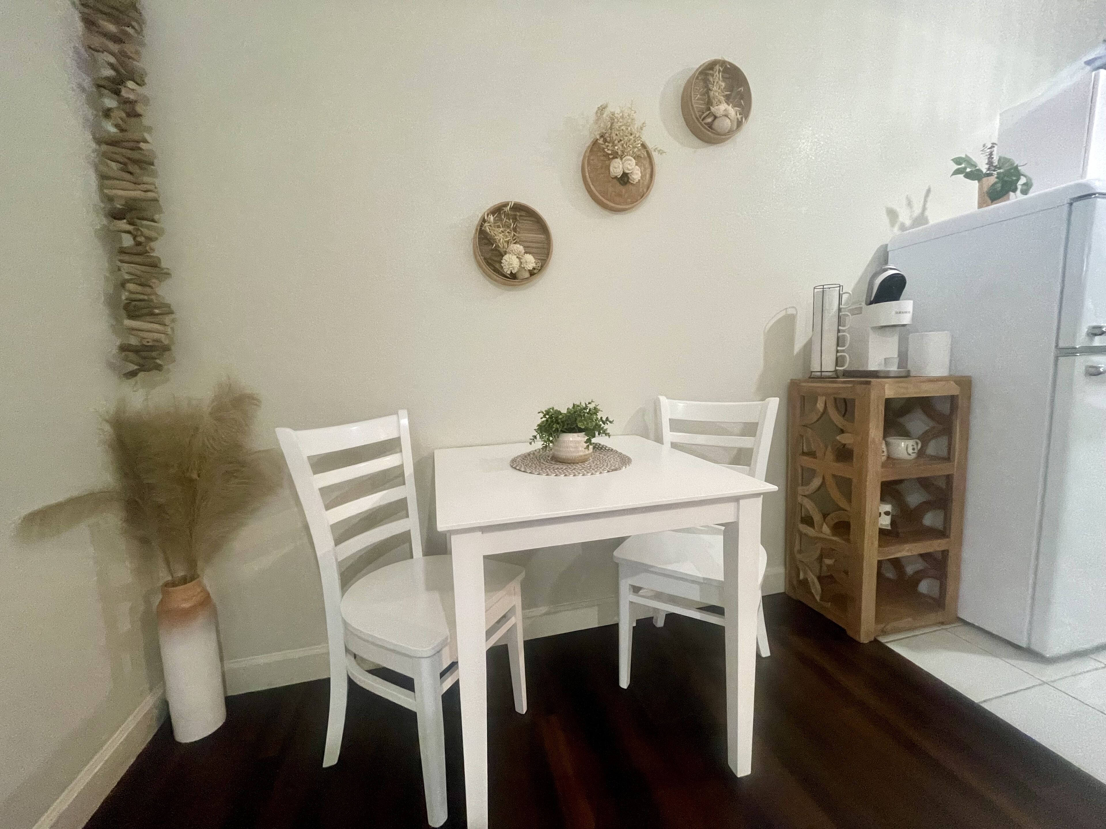A small dining area with a white table and chairs, a potted plant, and decorative wall art.