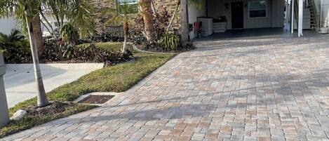 A residential driveway with a paved walkway leading to a house with a covered porch.