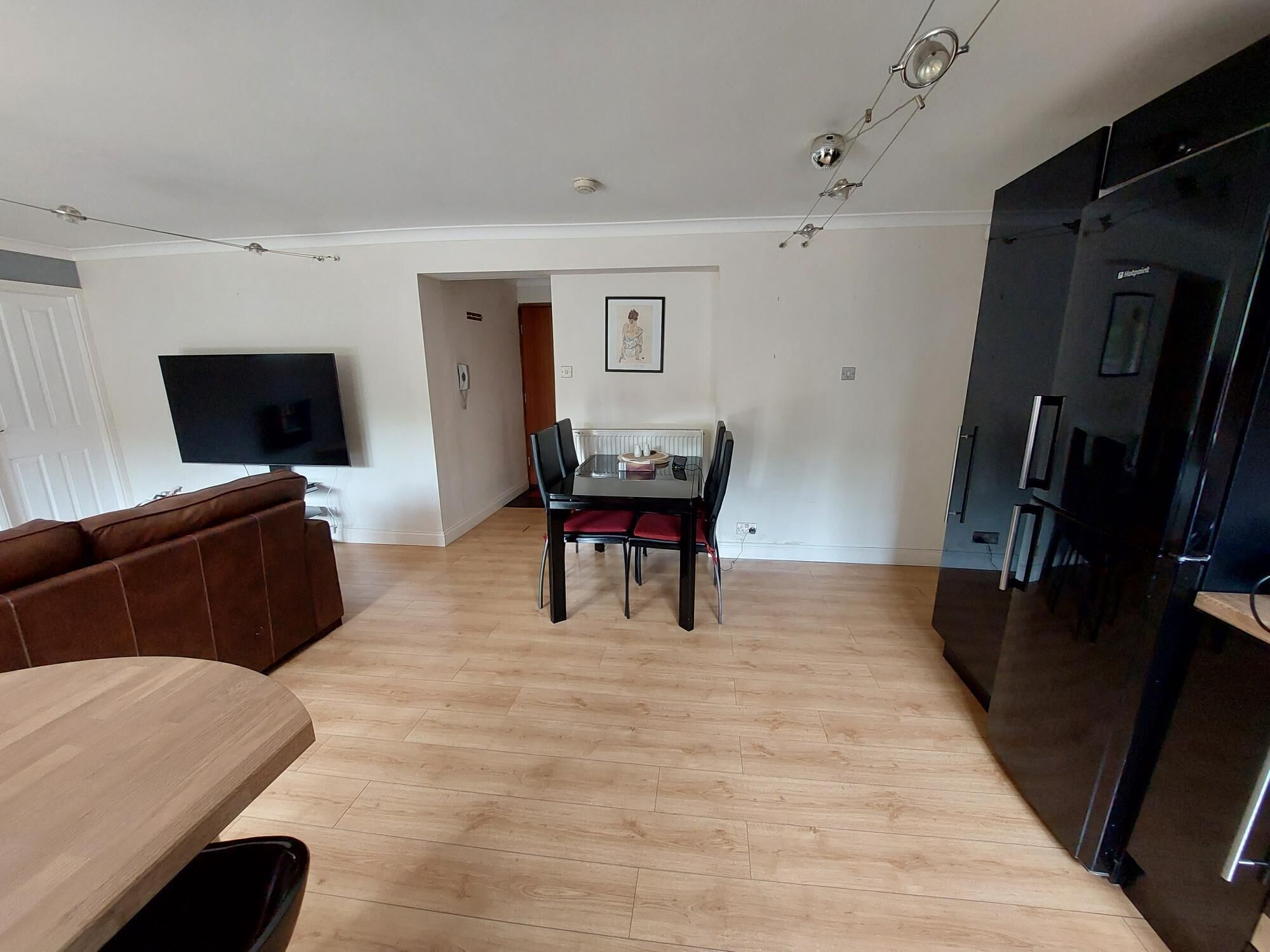 Eine moderne Küche mit einem schwarzen Kühlschrank, ein Essbereich mit Tisch und Stühlen sowie ein Wohnzimmer mit braunem Sofa und Flachbildfernseher.