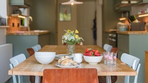 Een eettafel met een schaal aardbeien, een karaf en een bloevas.