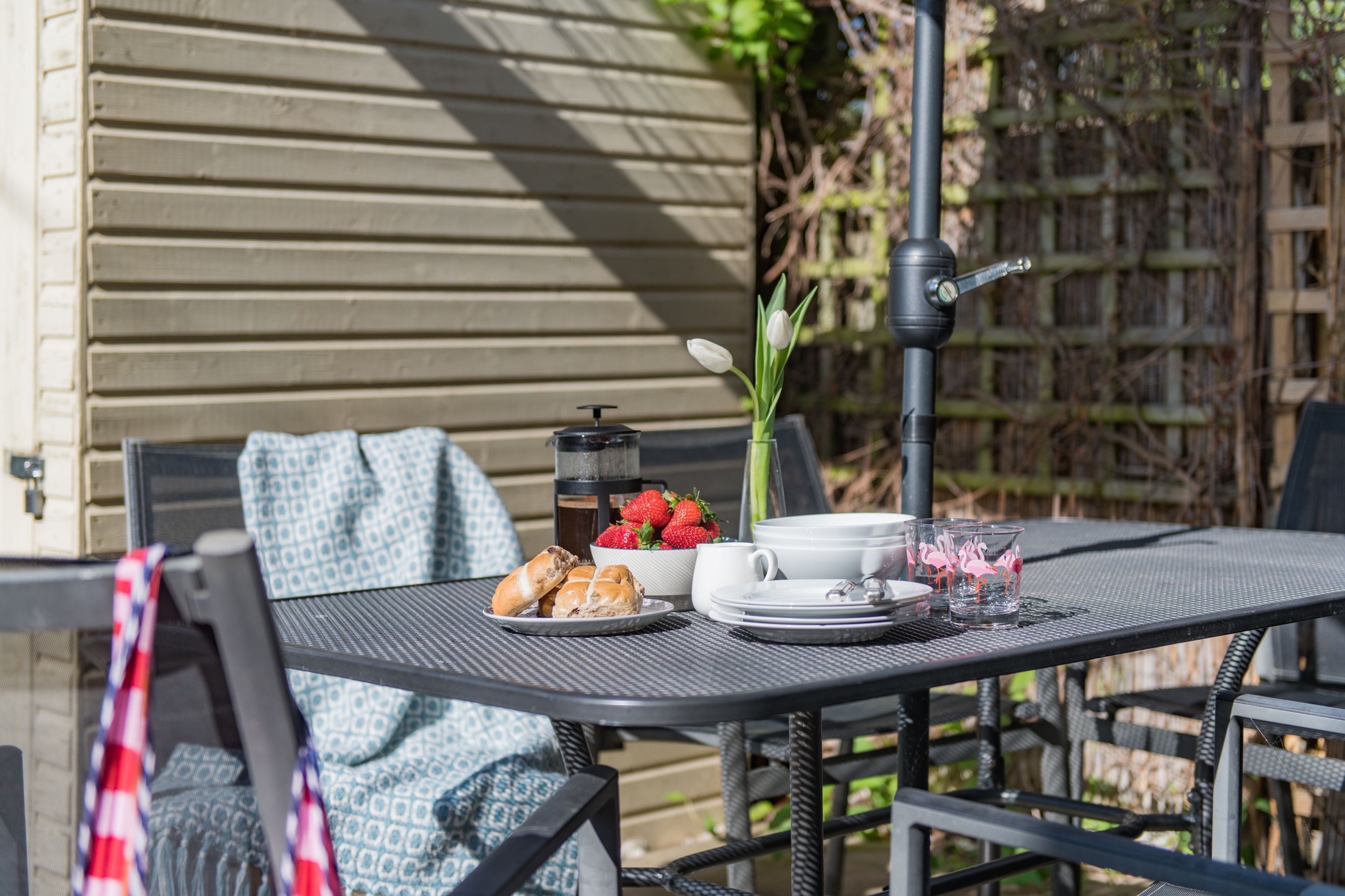 Une table à manger avec une machine à café, un bol de fraises, une assiette de croissants, une tasse et un verre décoré d’un motif de flamant rose.